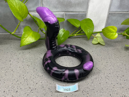 a purple and black snake laying on the ground next to a plant