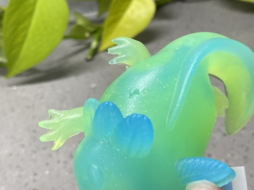 a green and blue toy lizard sitting on top of a piece of paper