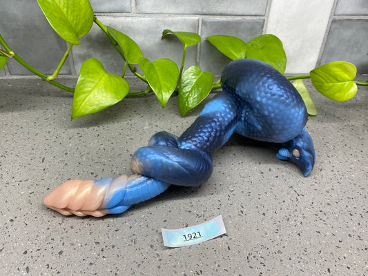 a blue and pink toy snake laying on the ground next to a plant