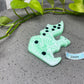 a green broccoli brooch sitting on a table next to a plant