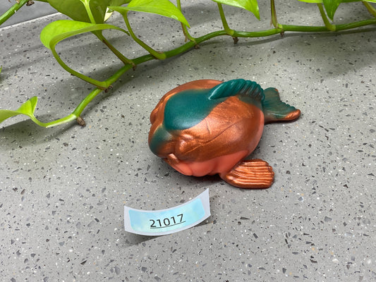 a small metal fish sitting on the ground next to a plant