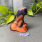 a small orange and black cat figurine next to a plant