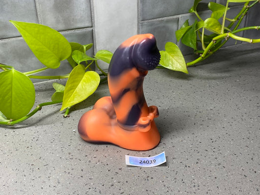 a small orange and black cat figurine next to a plant