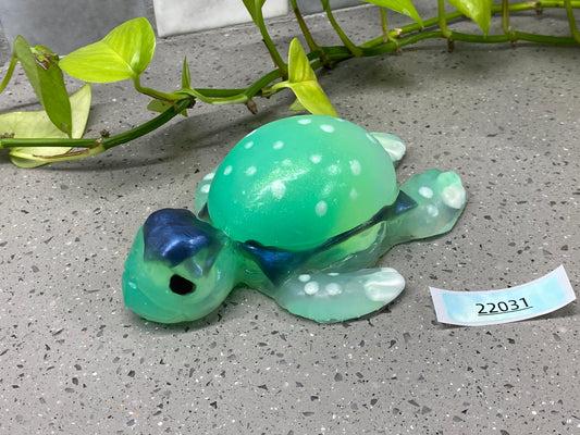 a green turtle figurine sitting next to a plant