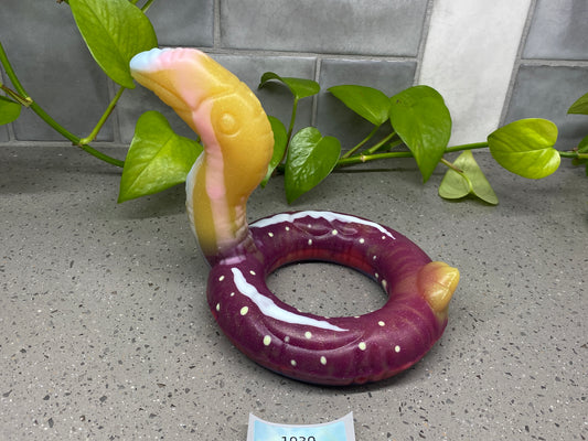 a purple doughnut sitting on top of a counter next to a plant
