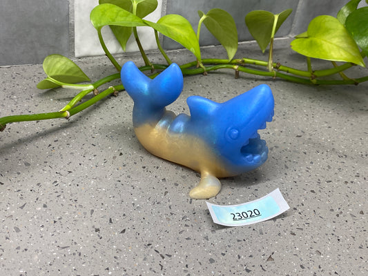 a blue and gold figurine laying on the ground next to a plant