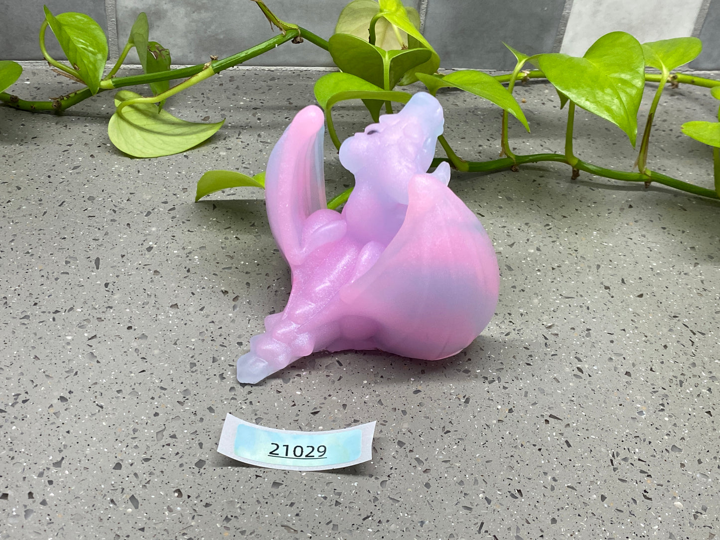 a plastic cat figurine sitting on the ground next to a plant