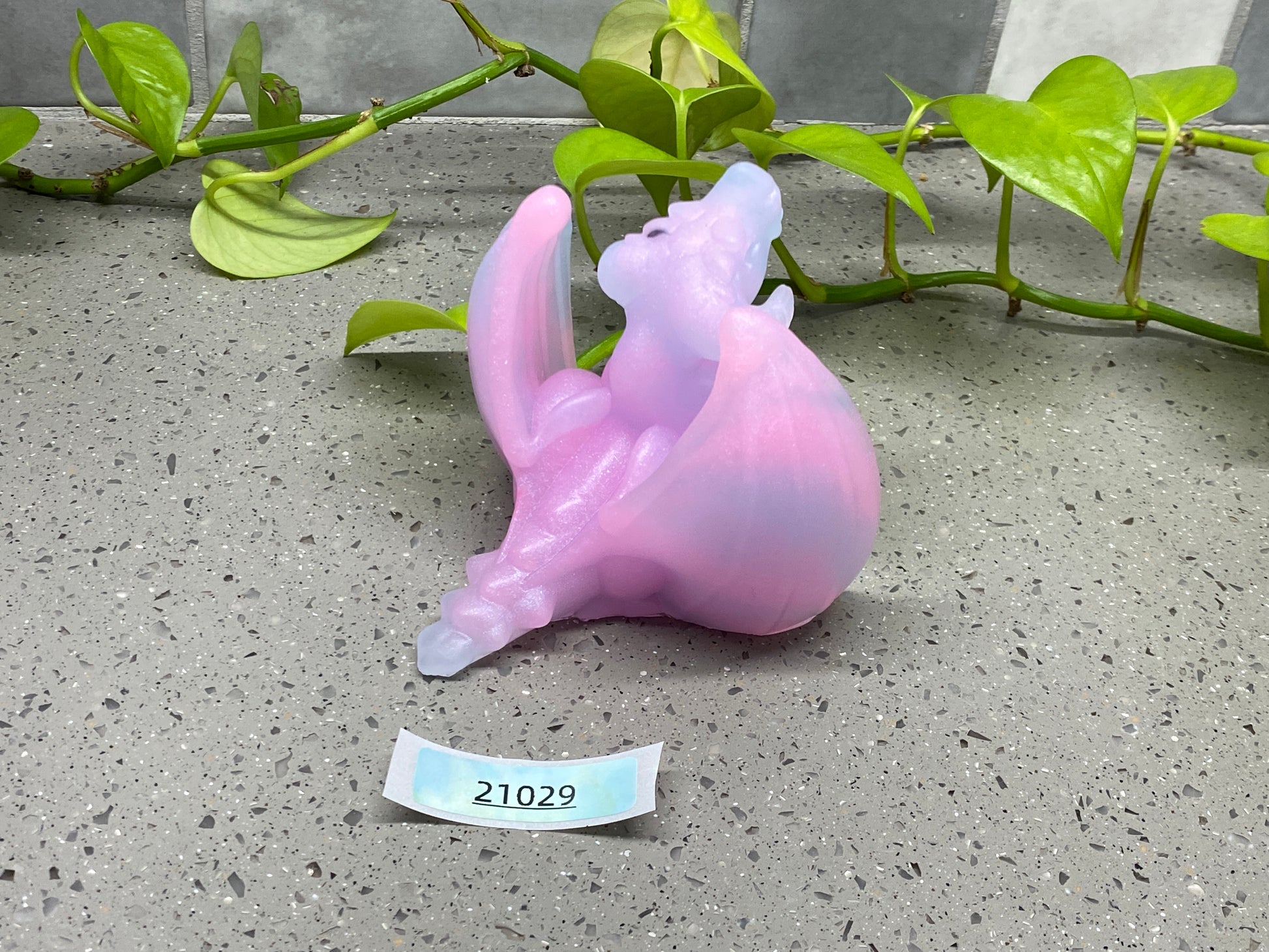 a plastic cat figurine sitting on the ground next to a plant