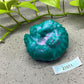 a green vase sitting on top of a cement floor next to a plant