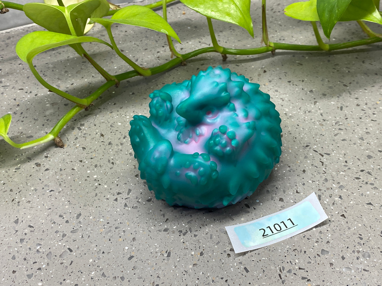 a green vase sitting on top of a cement floor next to a plant