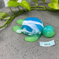 a blue and green turtle sitting on top of a cement ground