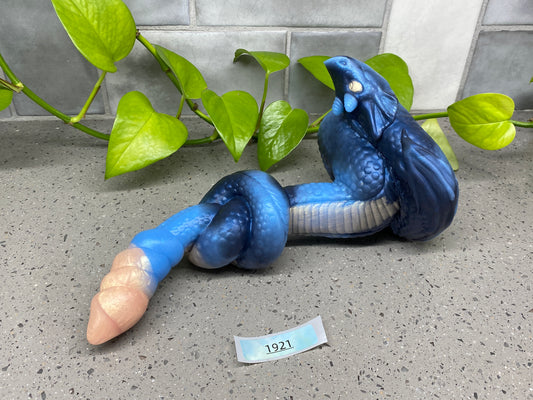 a blue snake figurine laying on the ground next to a plant