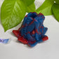 a blue and red frog figurine next to a green plant