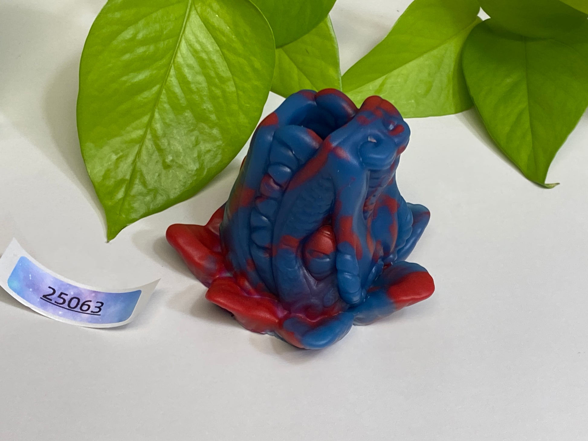 a blue and red frog figurine next to a green plant