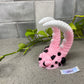 a pink and white giraffe shaped object next to a plant