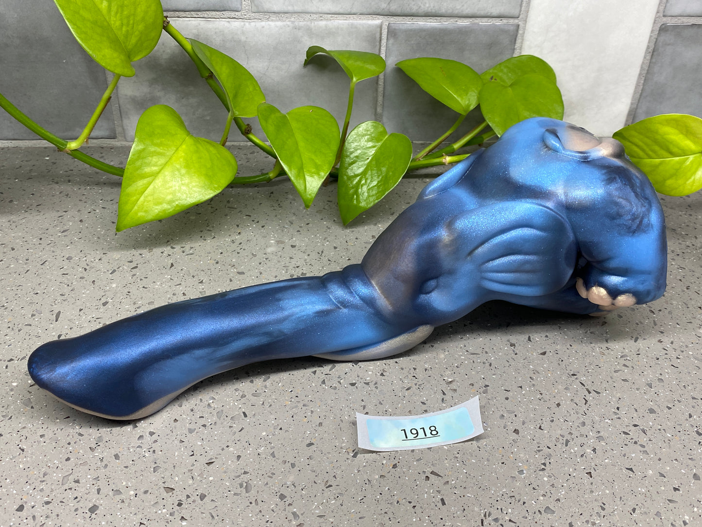 a blue statue of a cat laying on the ground next to a plant