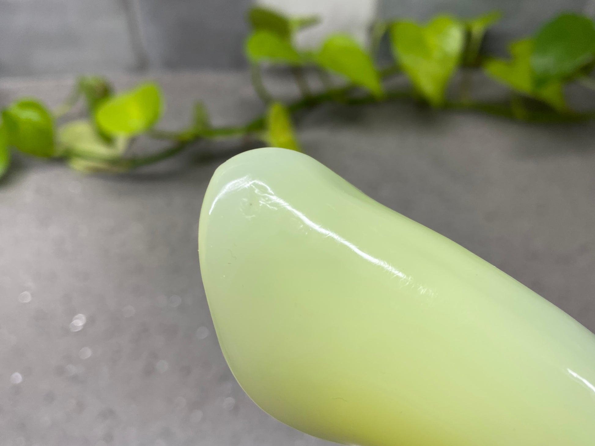 a close up of a green vase with a plant in the background