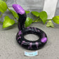 a purple and black snake laying on the ground next to a plant