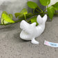 a small white figurine sitting next to a plant