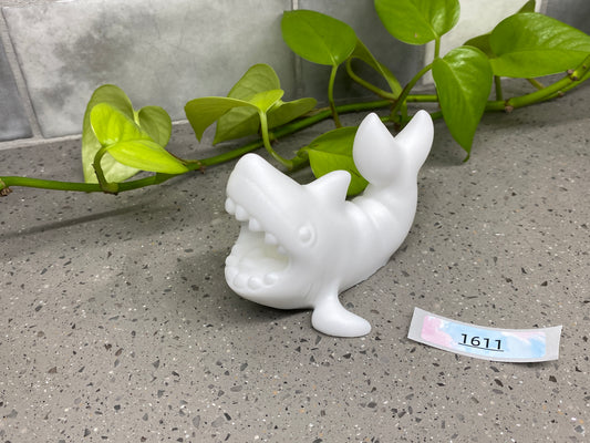 a small white figurine sitting next to a plant