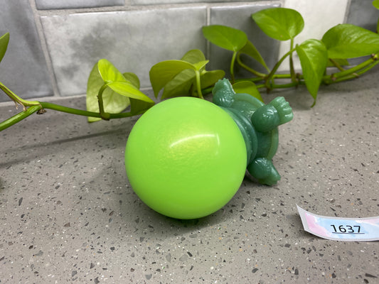a green toy turtle sitting on top of a green ball