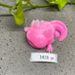 a pink toy lizard laying on the ground next to a plant