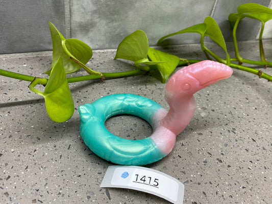 a pink and blue ring sitting next to a plant