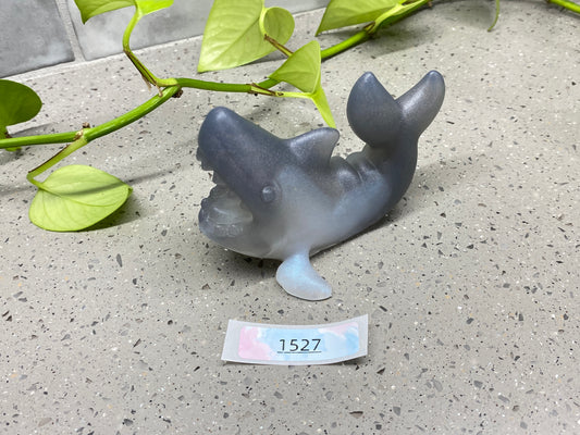 a small plastic dolphin on the ground next to a plant