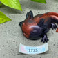 a small lizard figurine sitting on the ground next to a plant
