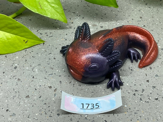 a small lizard figurine sitting on the ground next to a plant