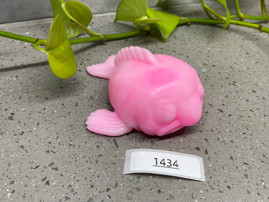 a pink plastic fish sitting next to a plant