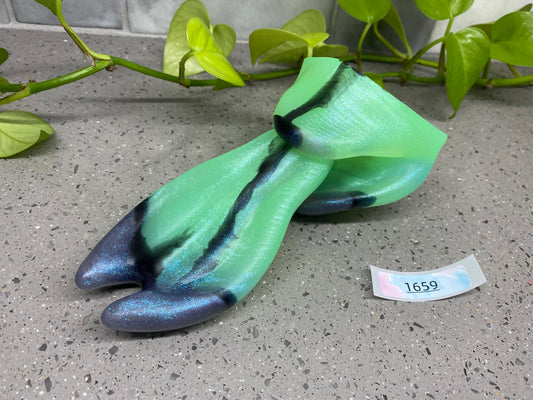a green and blue tie laying on the ground next to a plant