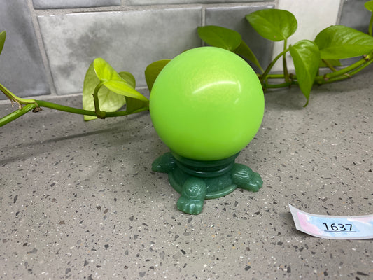a green vase sitting on top of a table next to a plant